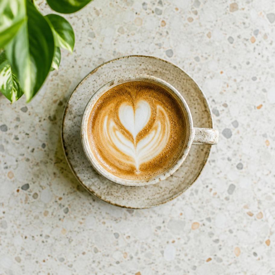 Cappuccino with heart latte art on a speckled ceramic saucer, photographed from above